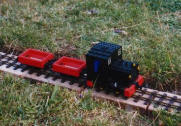 a garden railway train on track on a row of bricks laid in a trench on the lawn